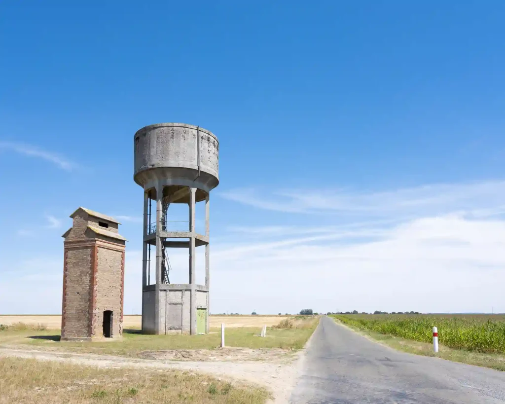 Rural French landscape with water tower and brick structure near a road.