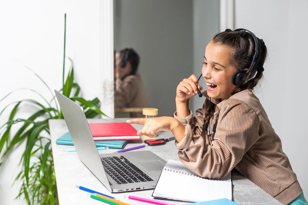 Happy girl with headset participates in online class, using laptop.